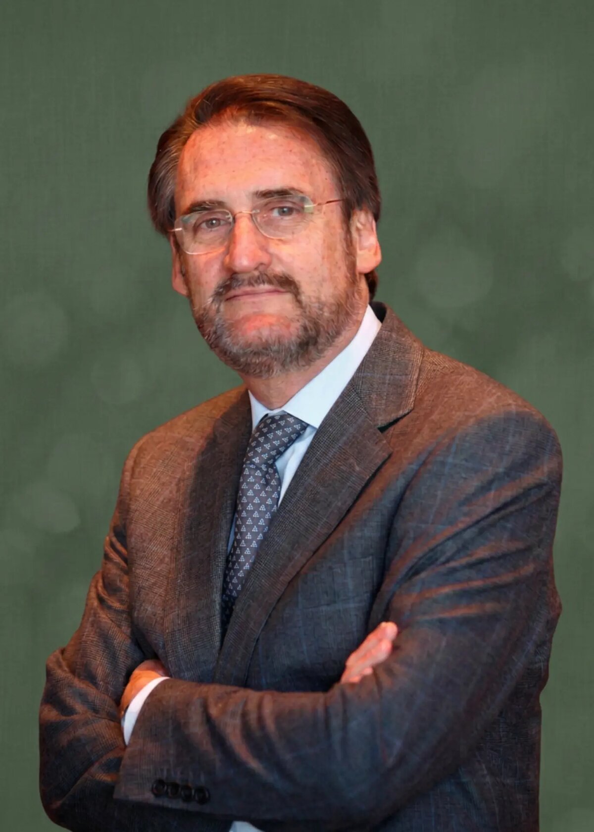 Retrato de Jaime Revilla Arroyo con traje gris y los brazos cruzados, sobre fondo verde